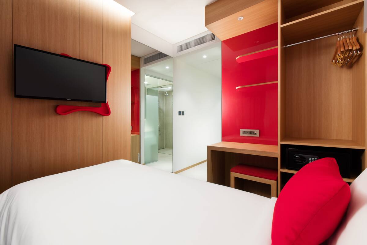 Une chambre d’hôtel moderne avec un grand lit, un téléviseur à écran plat fixé au mur et un mur d’accent de couleur rouge.
