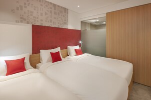 Una habitación de hotel moderna con dos camas, ropa de cama roja y blanca, un armario de madera y una pared con estampado.