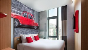 Ein Hotelzimmer mit einem großen Bett, einem Wandgemälde eines roten Autos, Blick auf Gebäude und einer roten Wanddekoration.