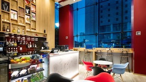Un espace bar moderne avec un présentoir de fruits, des étagères remplies de bouteilles et une vue sur le paysage urbain grâce à de grandes fenêtres.