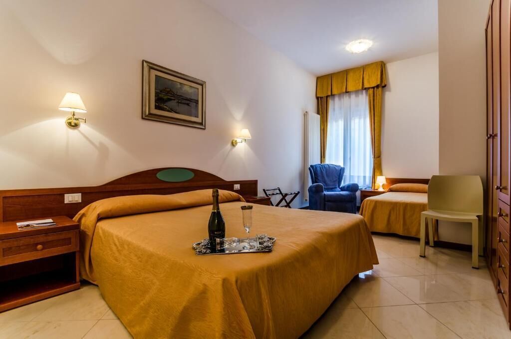A hotel room with two beds, a wooden headboard, a nightstand, a chair, a lamp, and a framed picture on the wall.