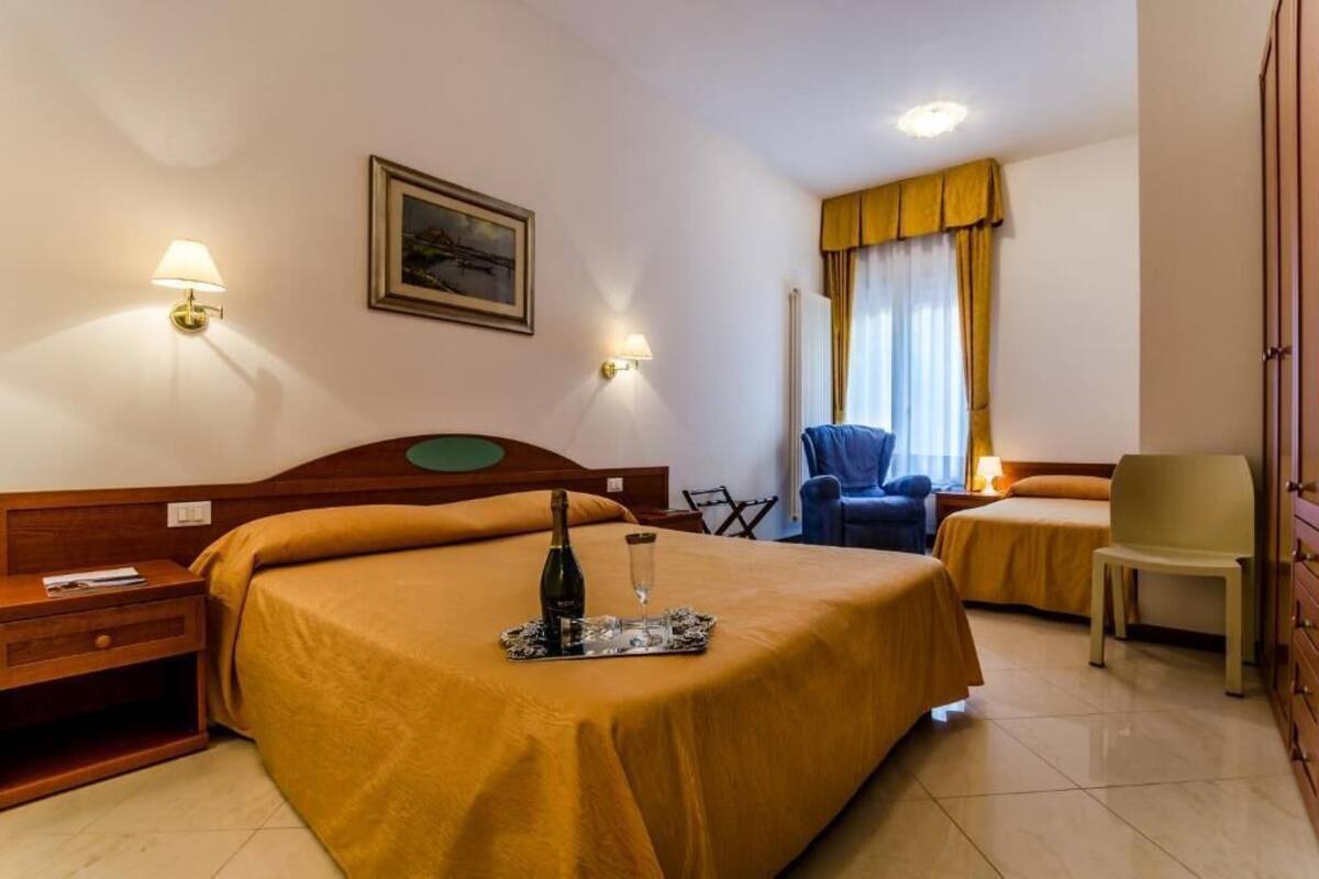 A hotel room with two beds, a wooden headboard, a nightstand, a chair, a lamp, and a framed picture on the wall.