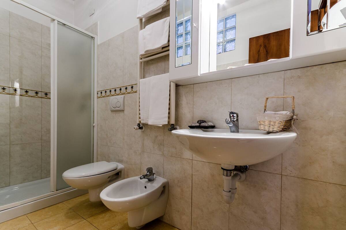 A bathroom with a glass shower enclosure, a toilet, a bidet, and a sink with a mirror above.