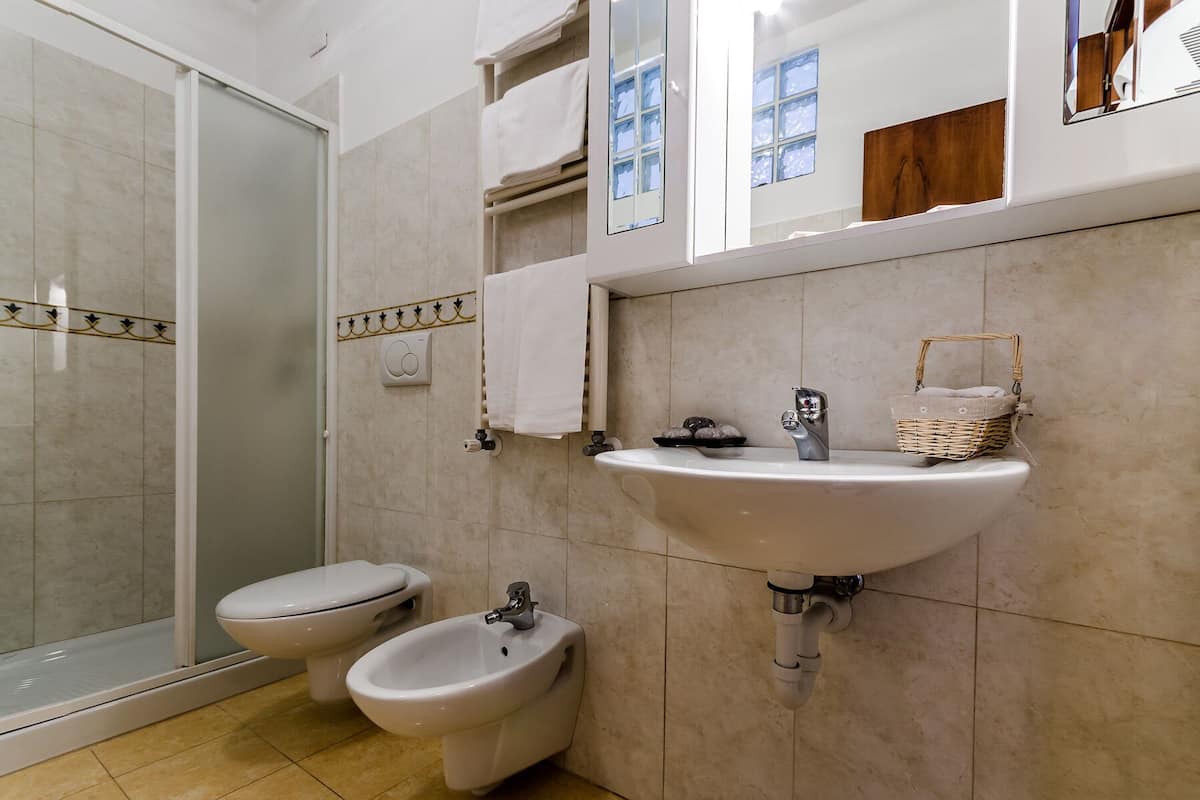 Un baño con cabina de ducha de vidrio, inodoro, bidé y lavamanos con espejo sobre él.