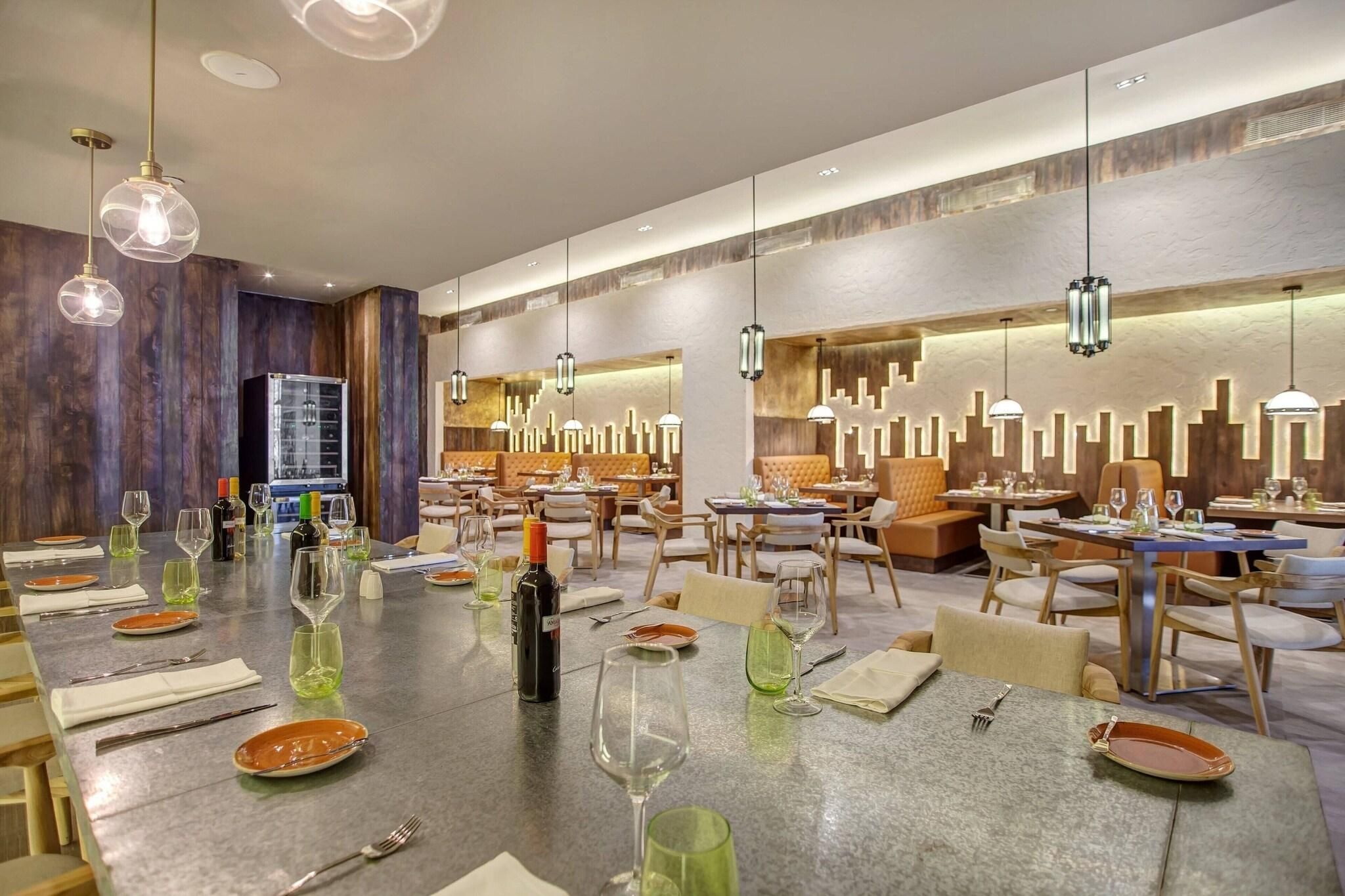 A restaurant with multiple dining tables set for service, a bar area, and a modern interior design with wooden accents and pendant lighting.