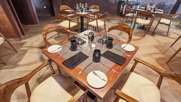 A dining area with wooden tables and chairs, each set with plates, cutlery, and glasses.