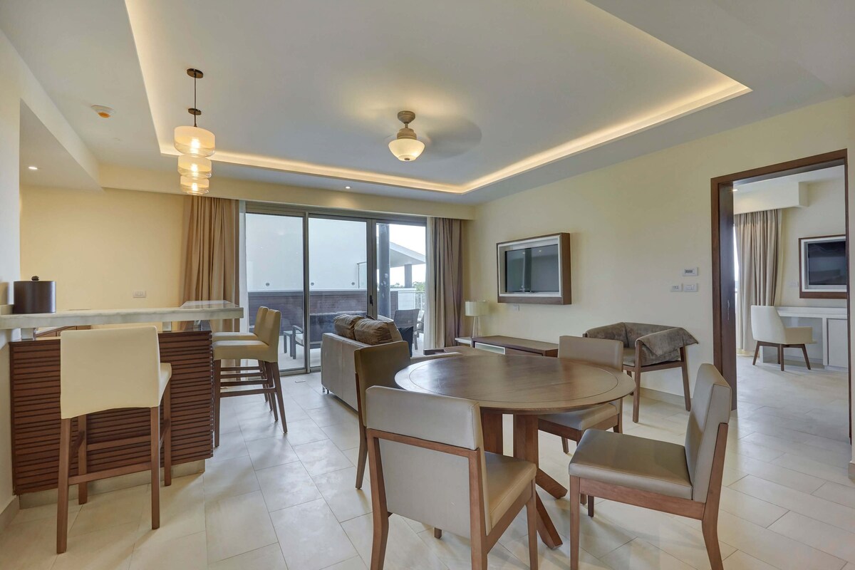A modern hotel room with a dining area, a living space, and a balcony with a view.