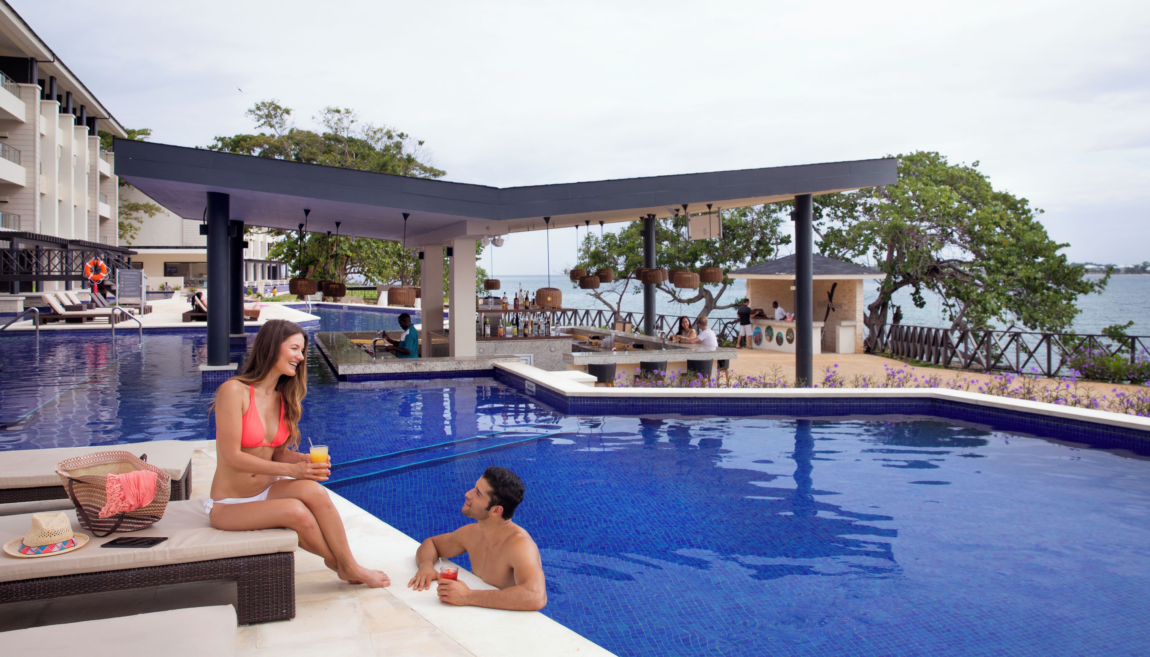 A poolside area with a bar, lounge chairs, and a view of the sea.