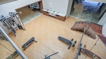A gym with exercise equipment, a reception desk, and a glass wall overlooking a wooden floor.