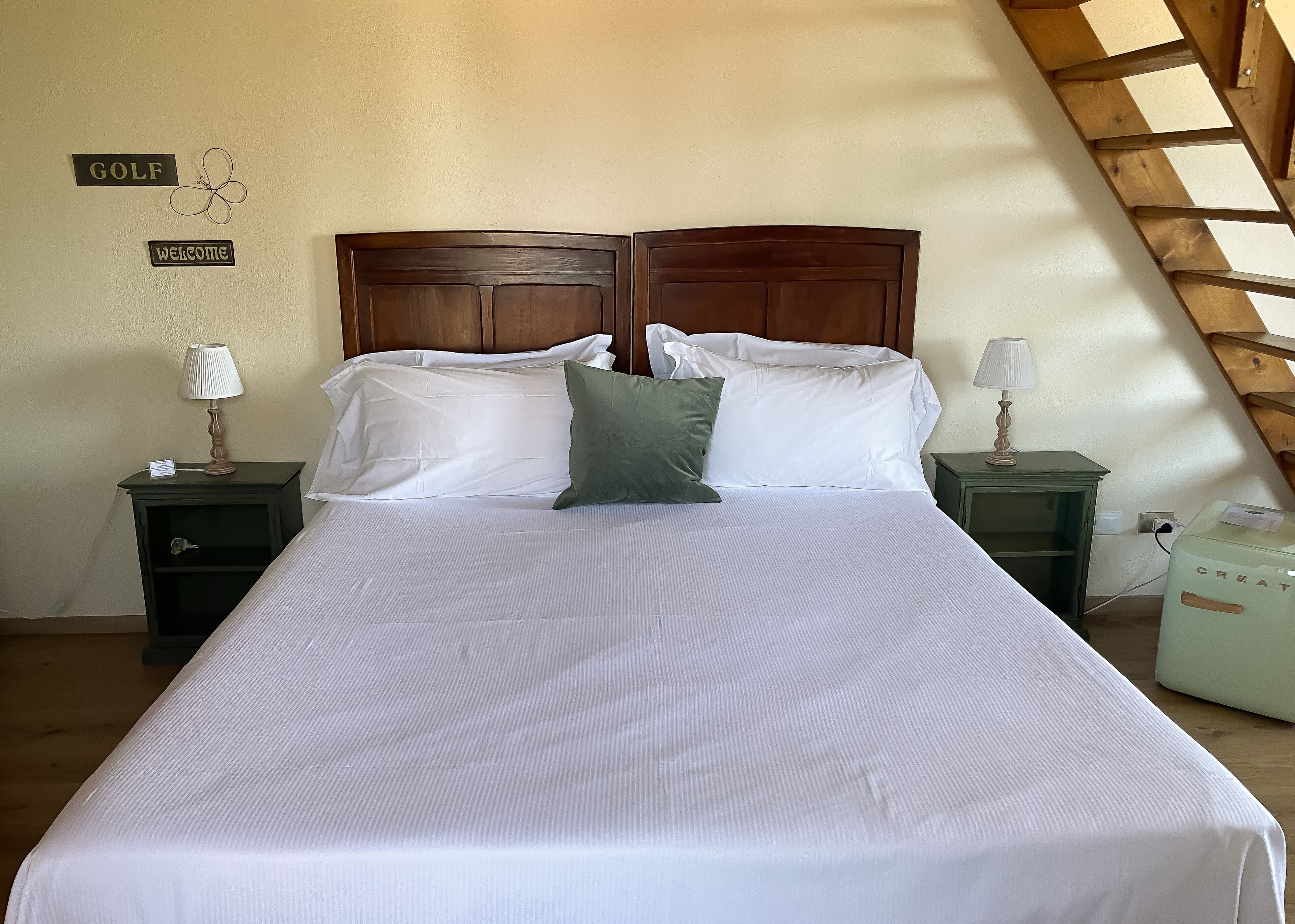 A neatly made bed with white linens, two bedside tables with lamps, and a wooden headboard.