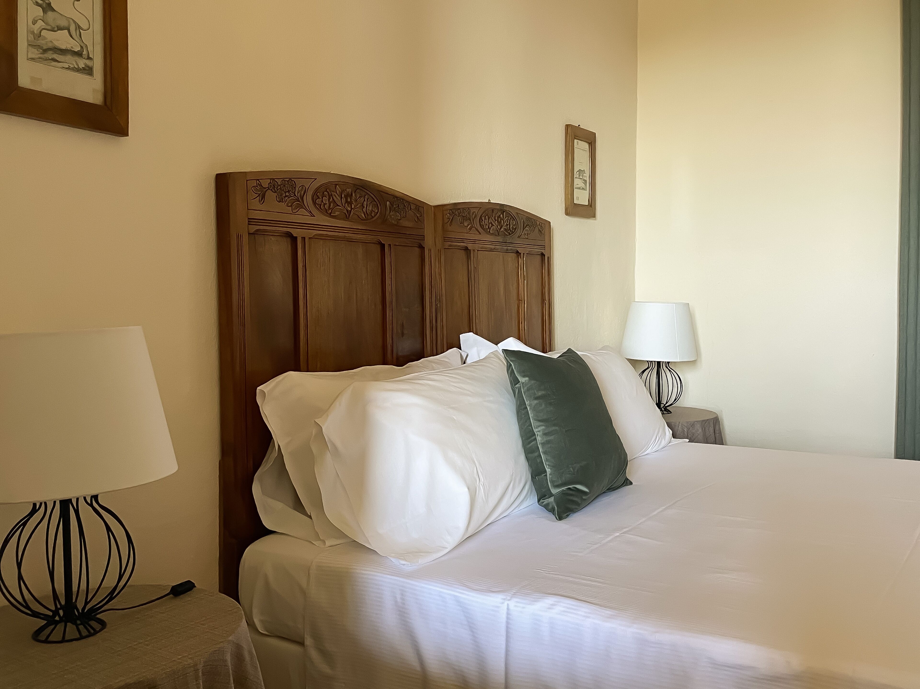 Un letto rifatto con cuscini bianchi e verdi, una testiera in legno e due lampade da comodino.
