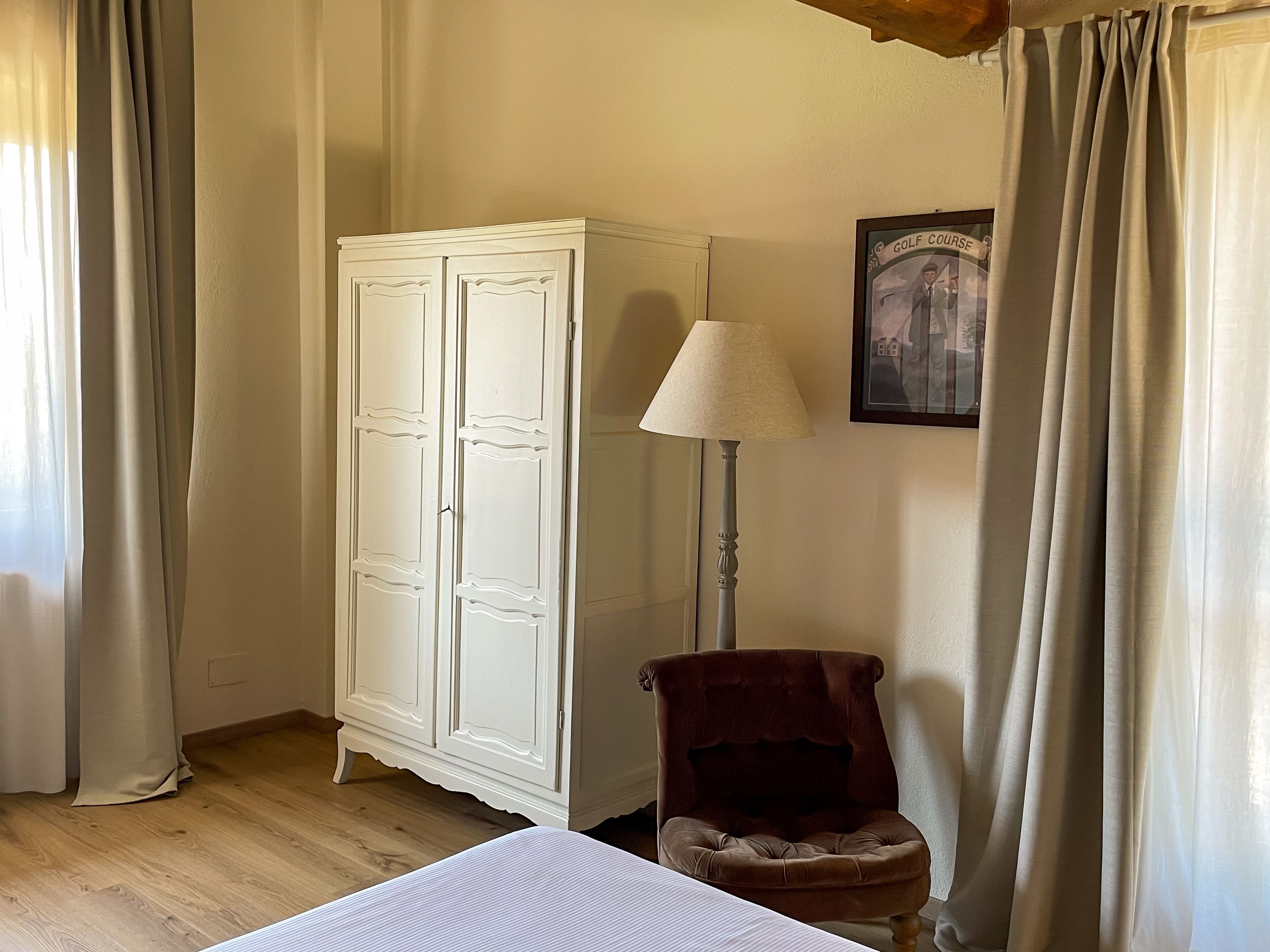 Una stanza con pavimento in legno, un armadio bianco, una poltrona marrone e una lampada.
