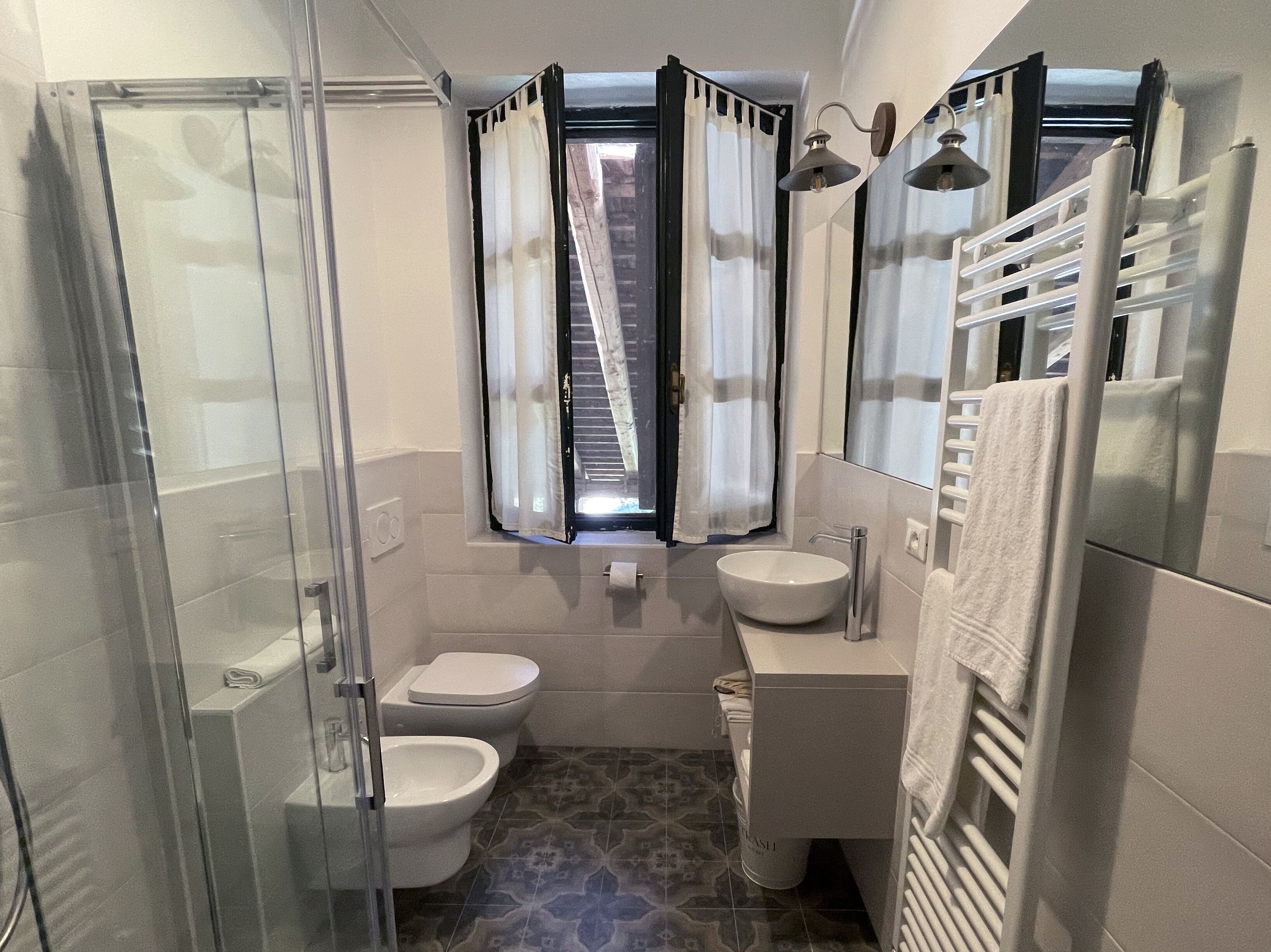 Un bagno compatto con cabina doccia in vetro, un WC, un bidet, un lavandino e un porta asciugamani.