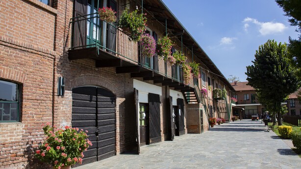 A brick building with multiple balconies, stone-paved ground, and potted plants.