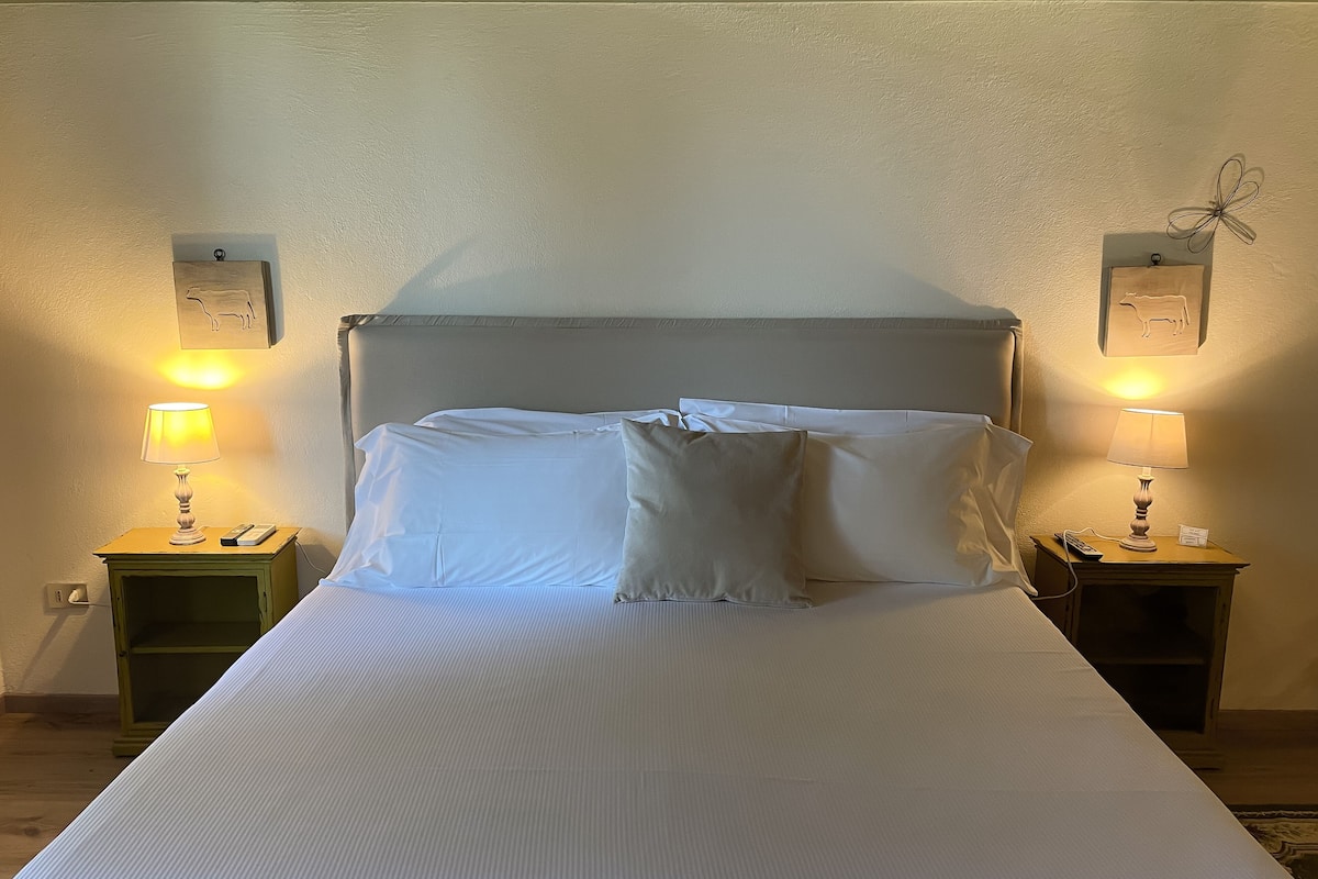 A neatly made bed with white linens and pillows, flanked by two bedside tables with lamps and a small decorative item on each.