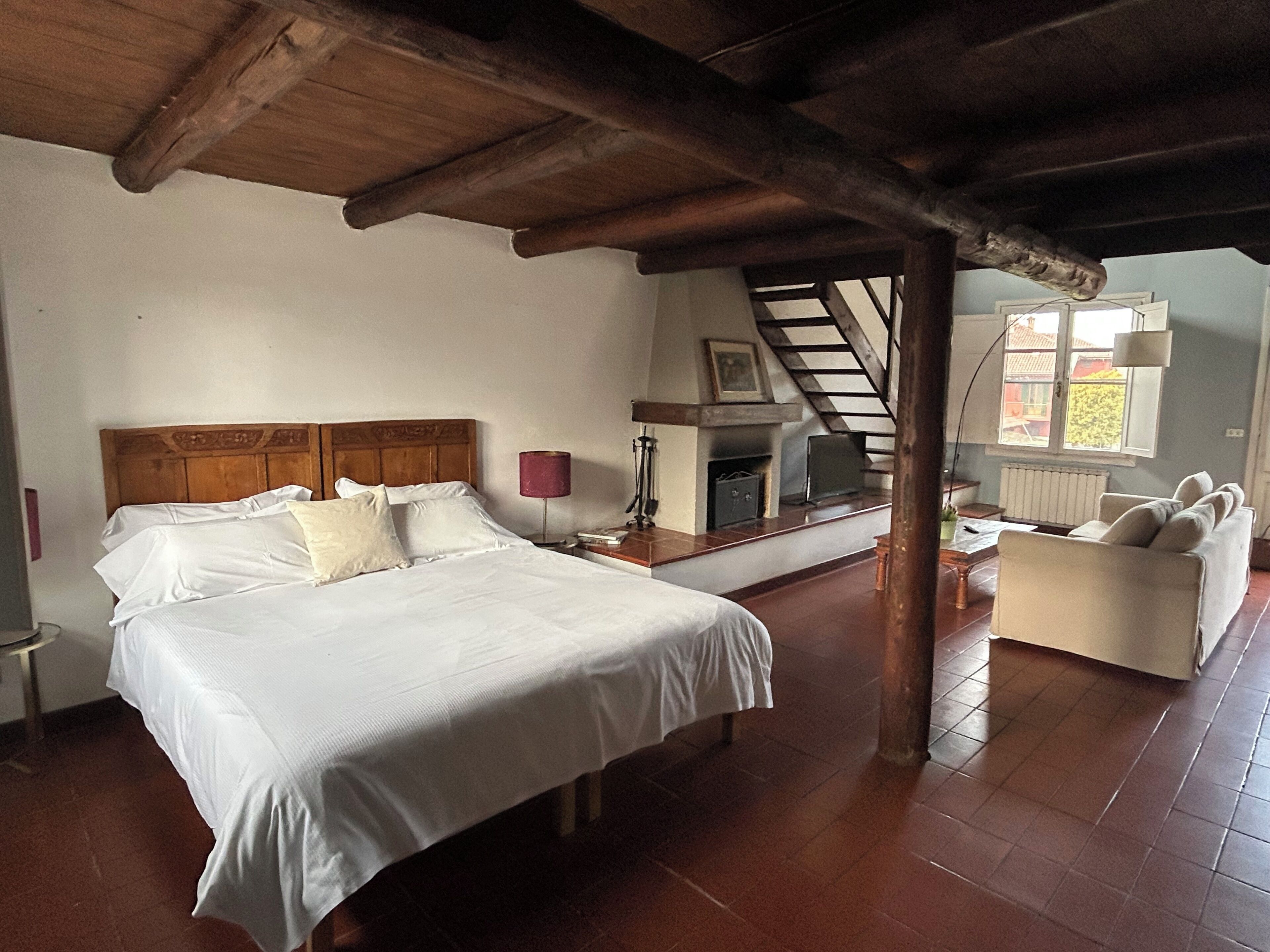 Un dormitorio con una cama grande, chimenea, sofá y vistas al exterior.