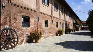 A brick building with a stone-paved courtyard, a large wooden wheel, and potted plants.