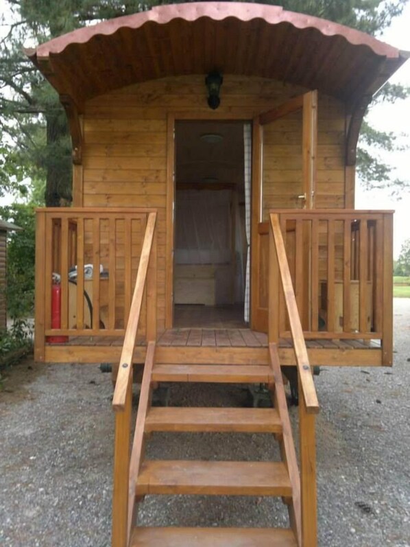 A wooden cabin with a porch, a staircase, and a fire extinguisher visible inside.