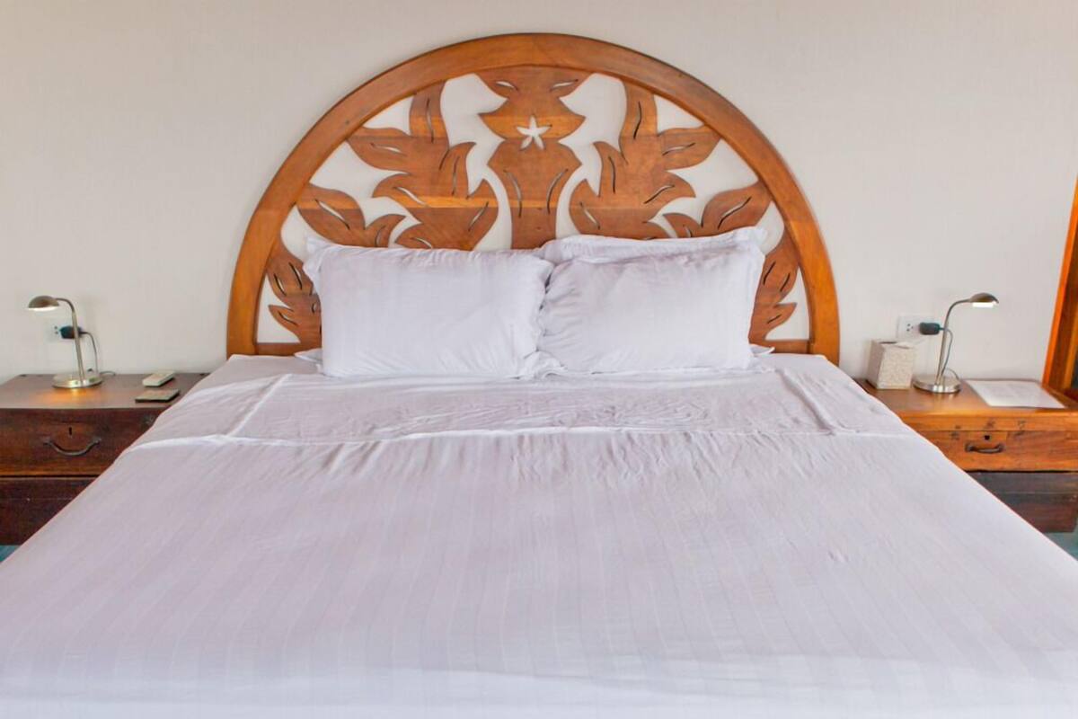 A neatly made bed with a wooden headboard, two bedside tables with lamps, and a wooden nightstand.