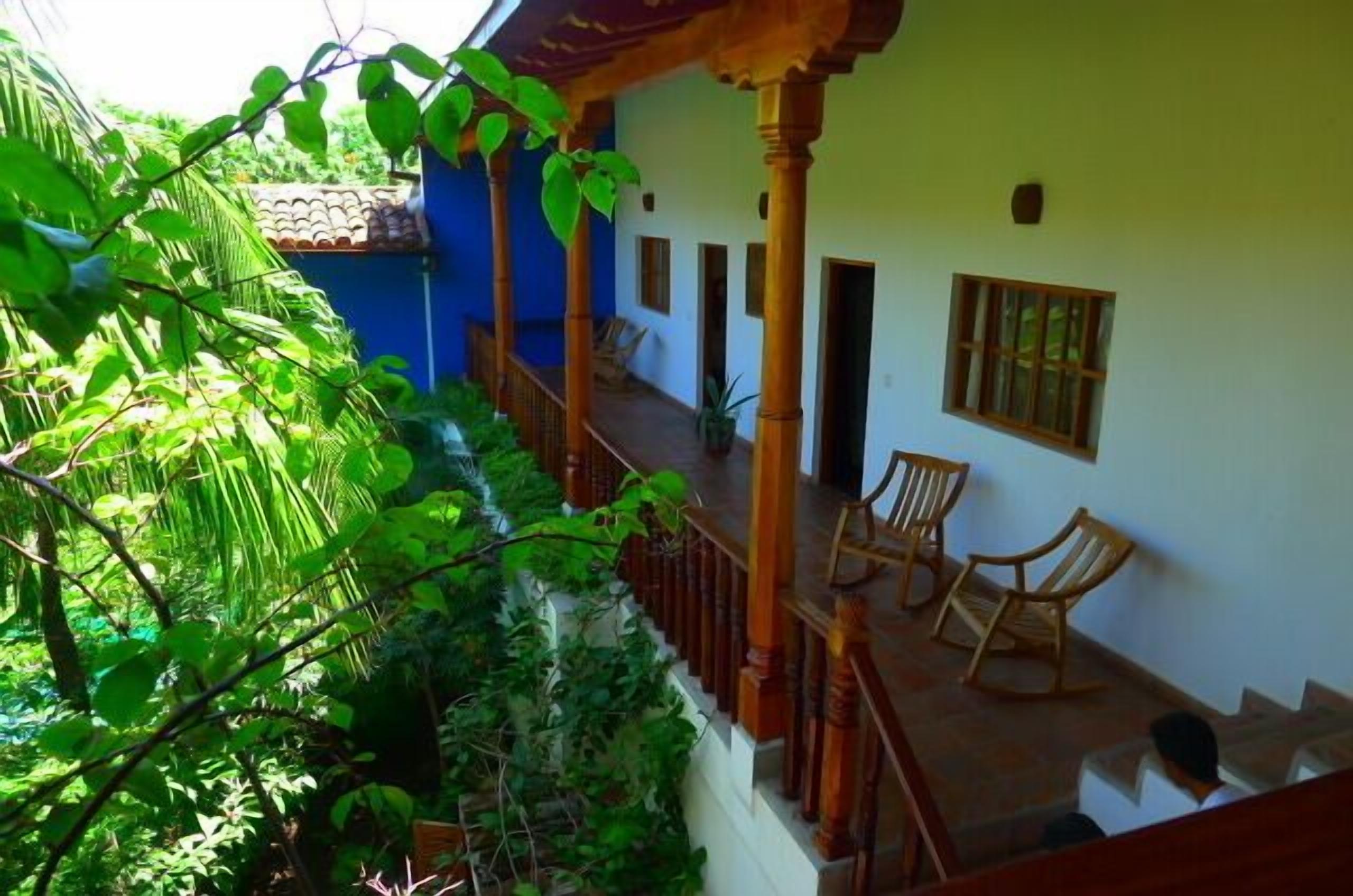A covered outdoor area with wooden chairs, a staircase, and a view of a lush garden.