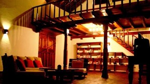Una sala de estar acogedora con una escalera de madera, un sofá con cojines rojos y una estantería llena de libros.