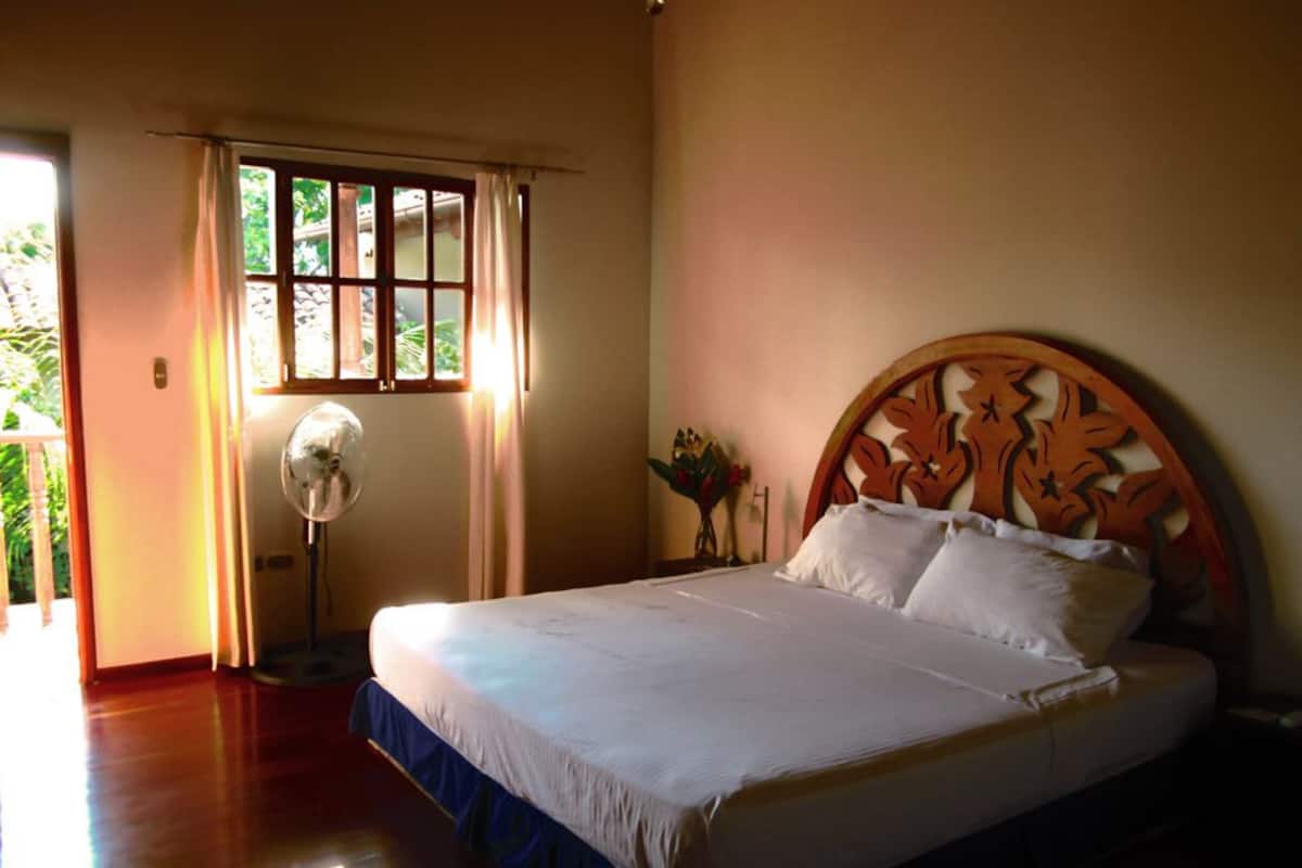 A bedroom with a bed, a fan, and a window with curtains.