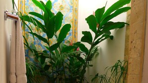 Un baño con piso de baldosas, un perchero y una planta grande en maceta.