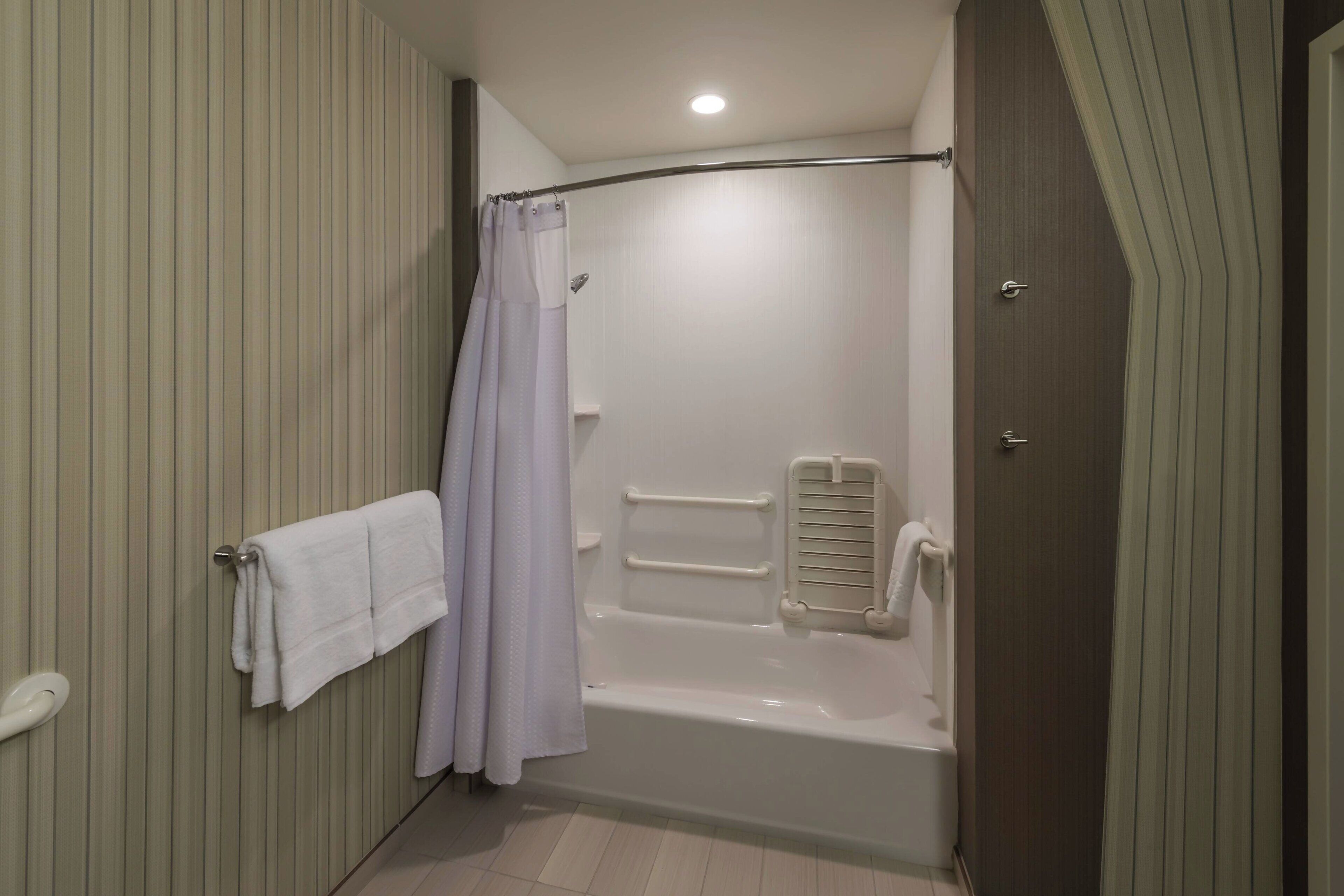 A bathroom with a bathtub, a shower curtain, a towel rack, and a handrail.