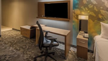 A hotel room with a desk, chair, bed, and a television mounted on the wall.