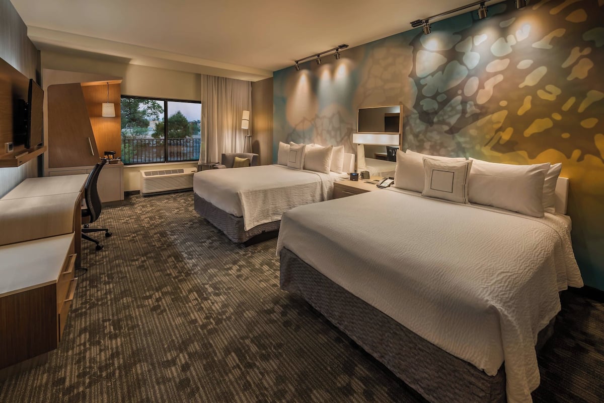 Quarto de hotel com duas camas, uma escrivaninha, uma cadeira, televisão e janela com cortinas.