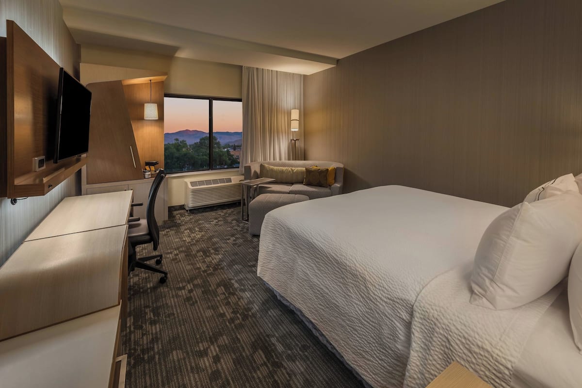 Quarto de hotel com uma cama grande, uma escrivaninha, uma cadeira, uma televisão e uma janela com vista para as montanhas.