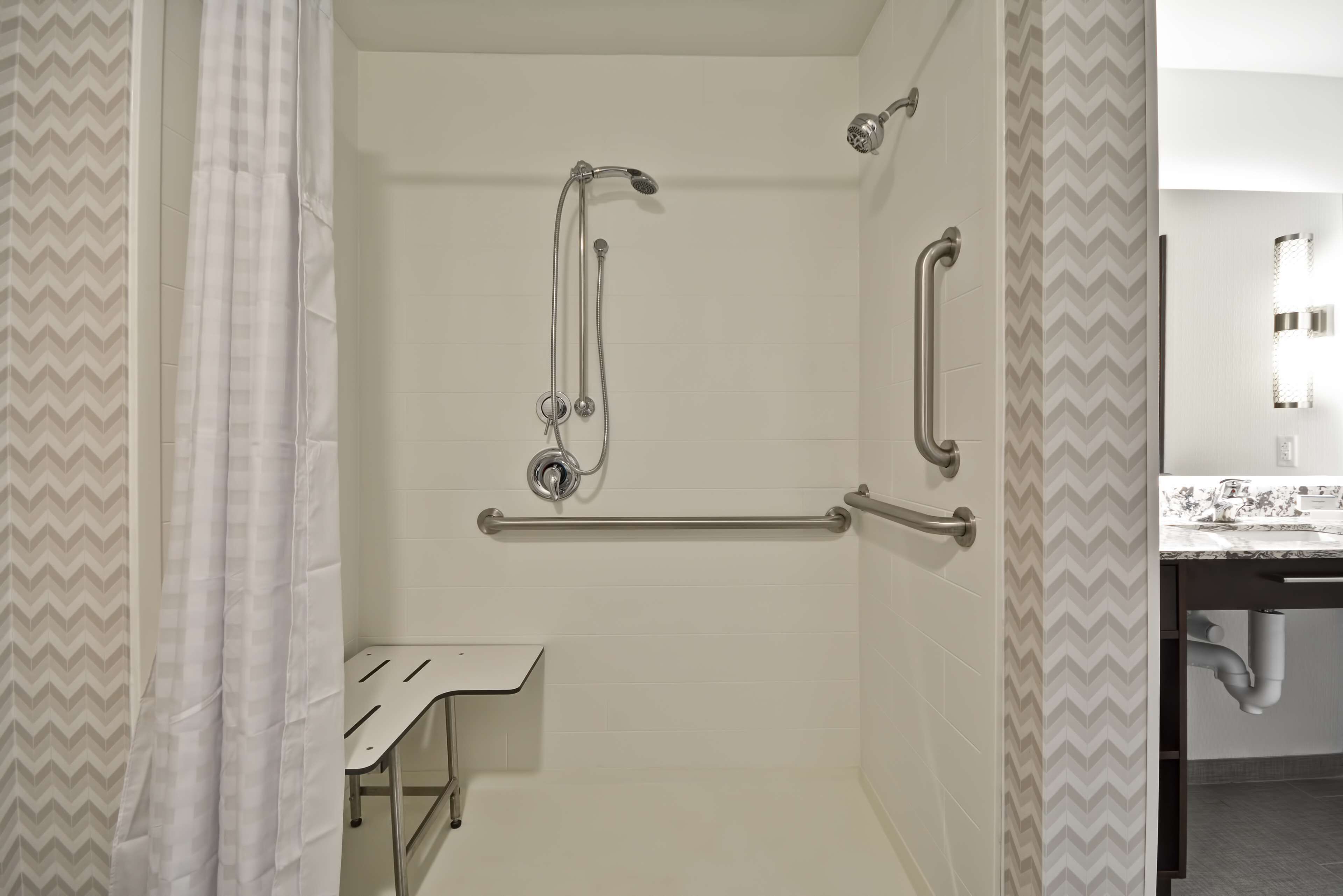 A shower with grab bars, a white sink, and a mirror.