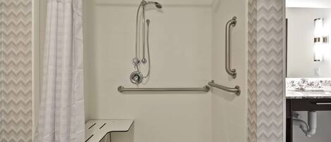 A shower with grab bars, a white sink, and a mirror.