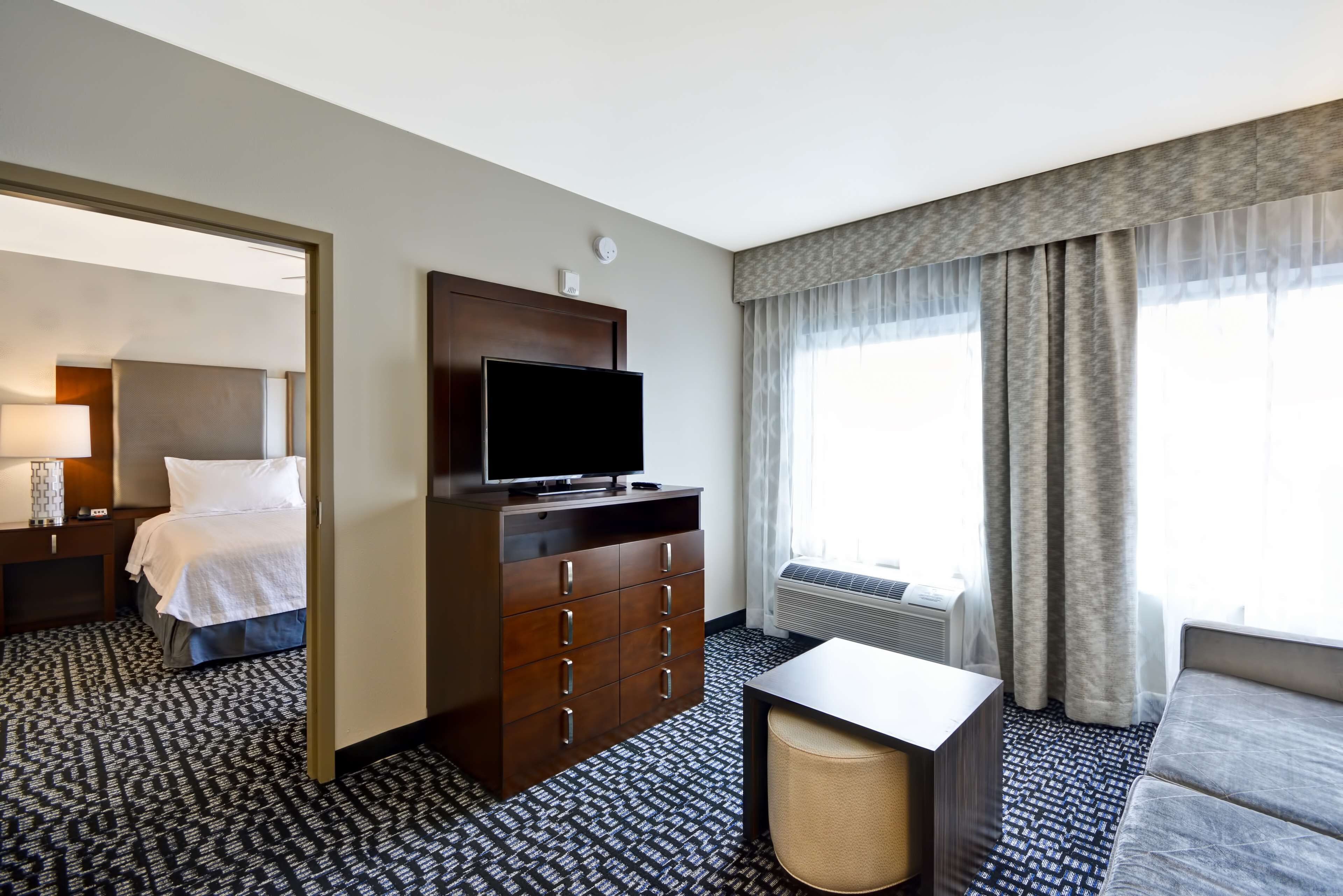 A hotel room with a bed, a TV on a dresser, a desk, and a window with curtains.