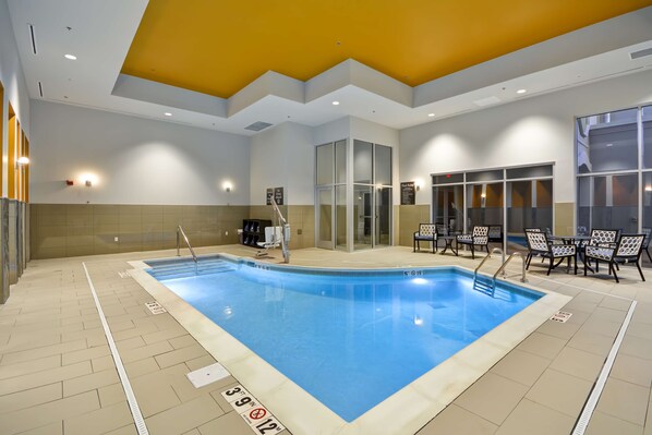 Piscina interior con carriles delimitados, vestuario y zona de estar con sillas.