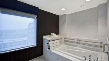 A modern bathroom with a large bathtub, a window with blinds, and marble walls.