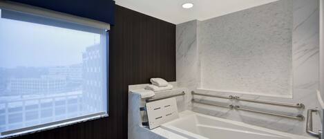 A modern bathroom with a large bathtub, a window with blinds, and marble walls.