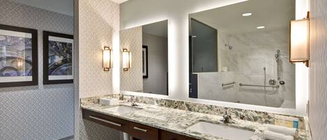 A modern bathroom with a large mirror, two sinks, marble countertops, and wall-mounted sconces.