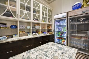 A kitchen with dark cabinets, a marble countertop, and a refrigerator stocked with beverages.