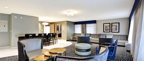 Une chambre d’hôtel moderne dotée d’un coin repas, d’un ensemble de canapés et d’une moquette à motifs.