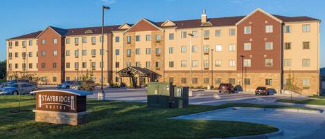 A multi-story hotel with a central entrance, parking area, and a sign indicating the hotel name.