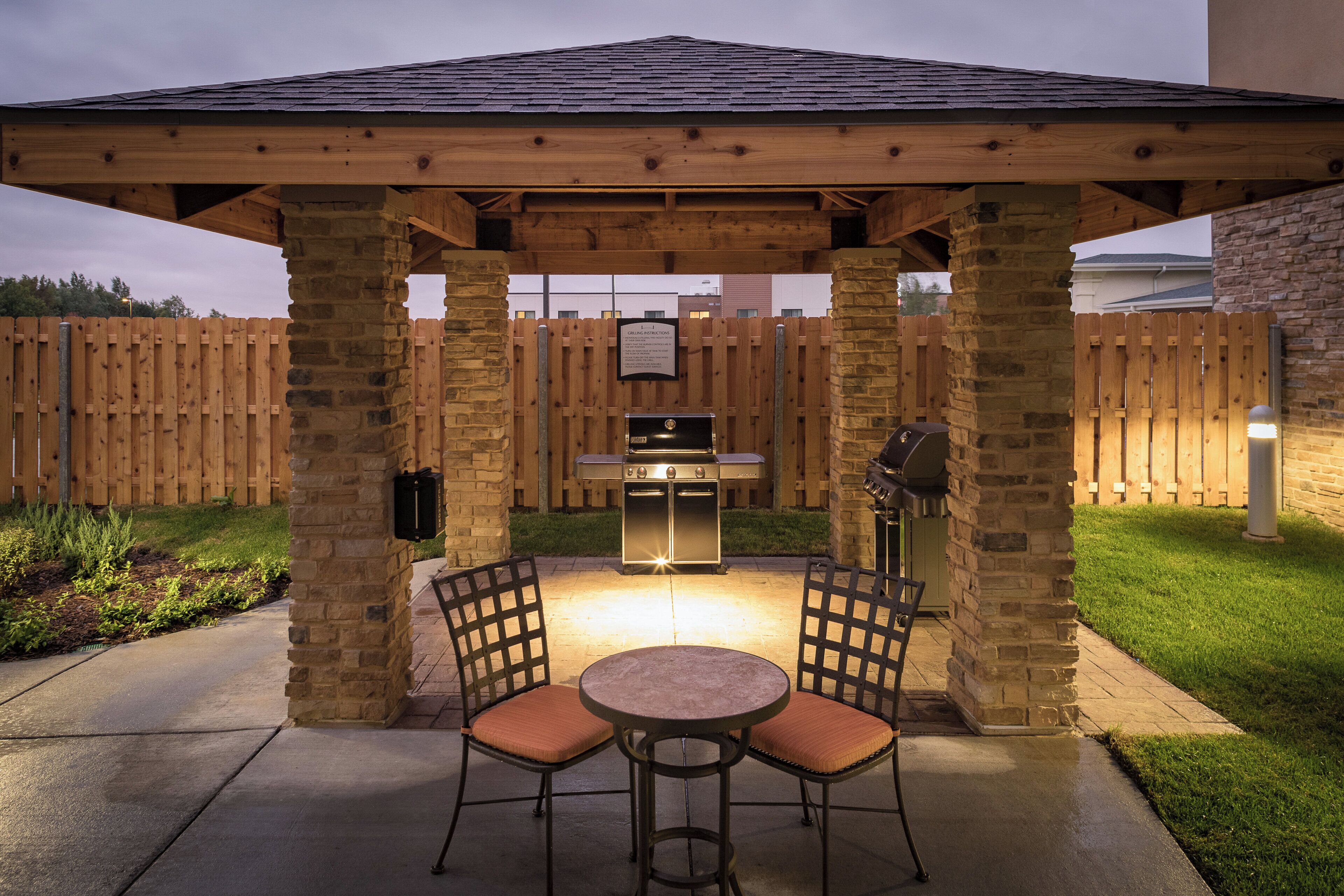 Une terrasse extérieure dotée d’un espace barbecue couvert, de piliers en pierre et de deux chaises.