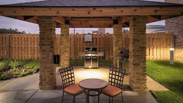 Une terrasse extérieure dotée d’un espace barbecue couvert, de piliers en pierre et de deux chaises.