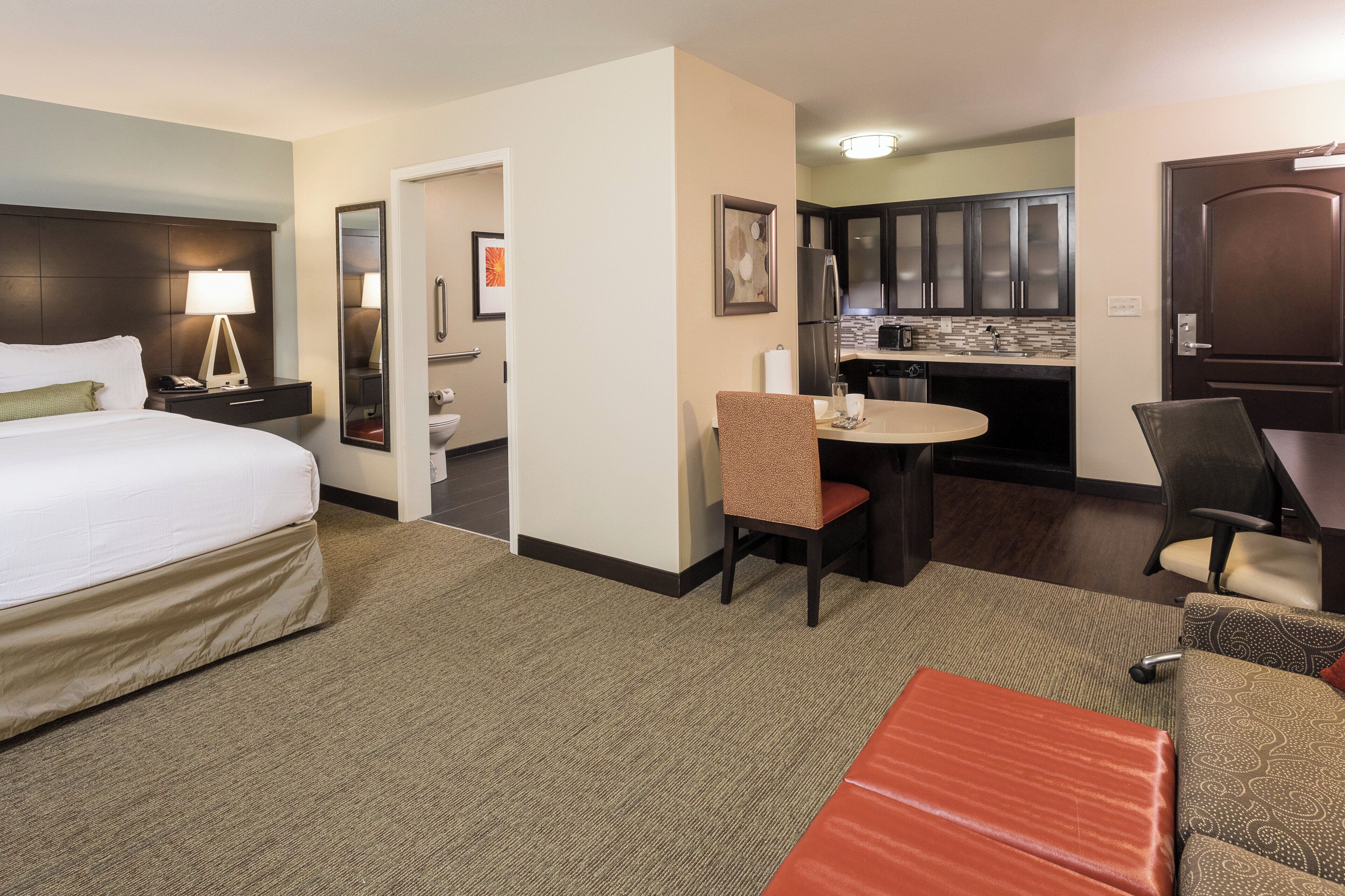 Een hotelkamer met een bed, bureau, stoel, klein tafeltje en kitchenette.