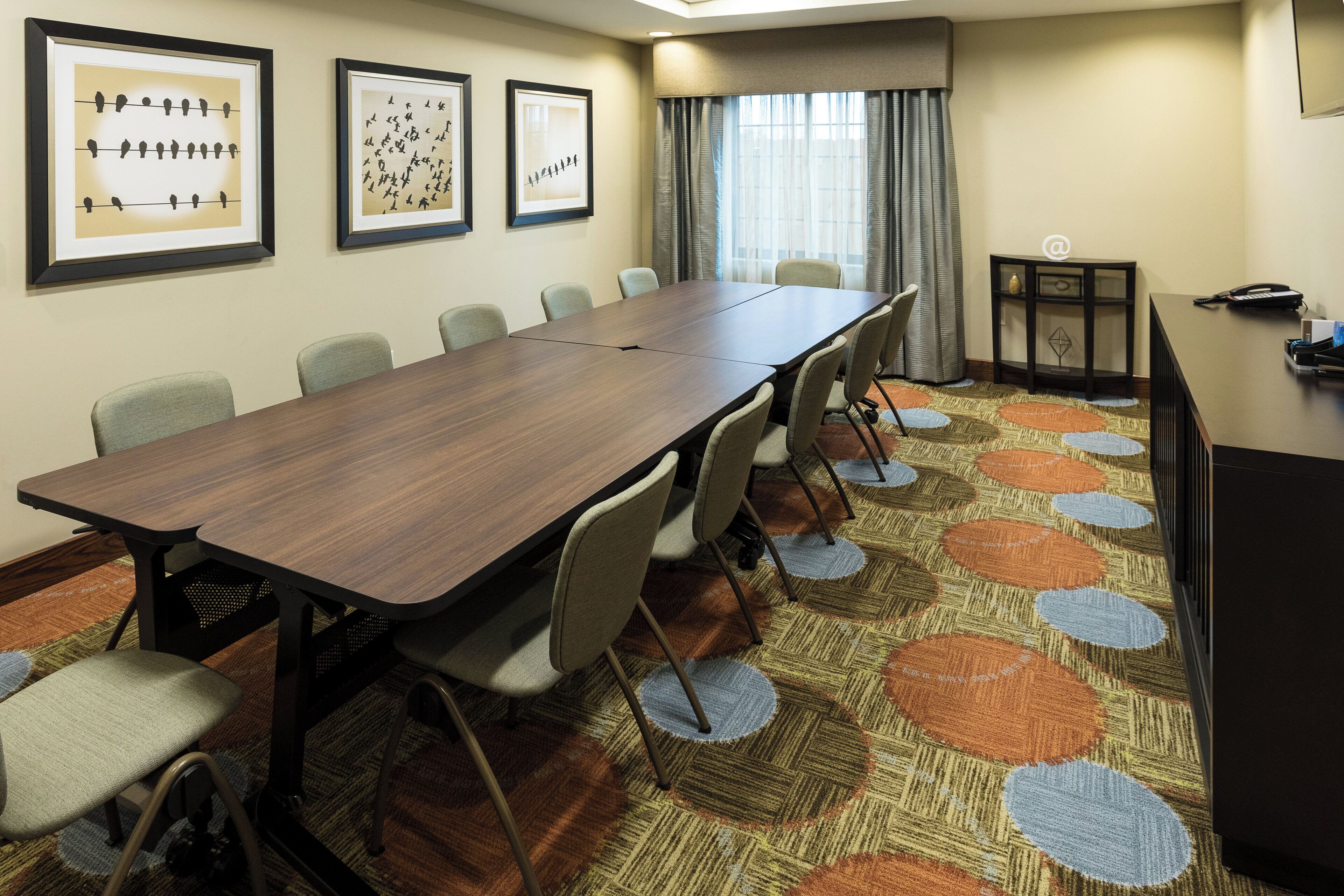 A conference room with a long table, chairs, framed artwork on the wall, and a desk with a phone.
