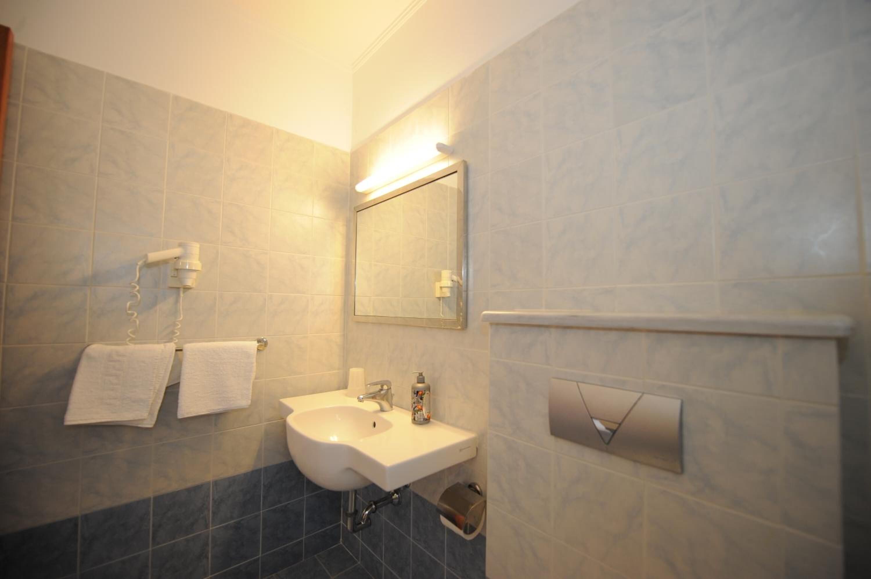 A bathroom with a sink, mirror, towel rack, and a soap dispenser.