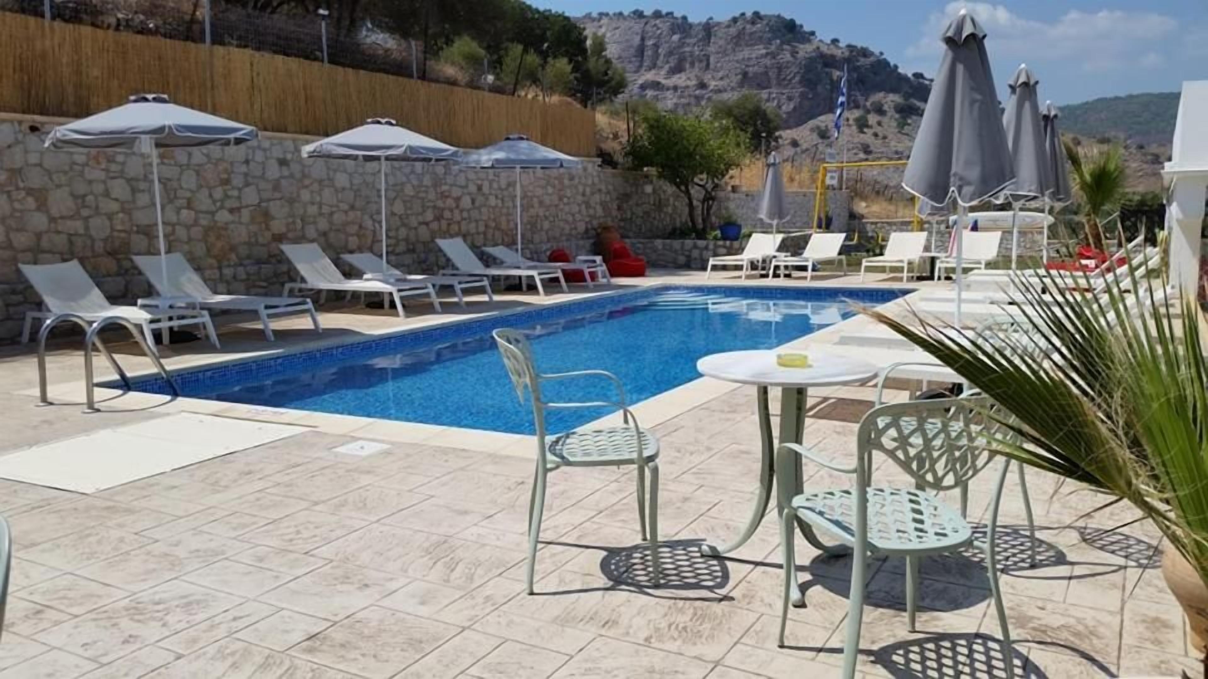 Zona de piscina con sillones reclinables y sombrillas, una pared de piedra y vistas a las colinas.