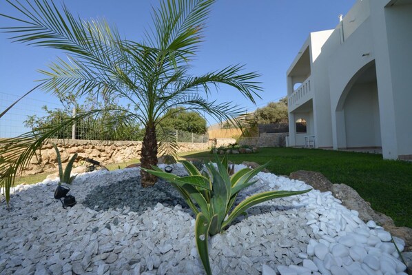 A landscaped garden with a palm tree, white pebbles, and a white building with arches. - Golden View Studios (Rhodes)