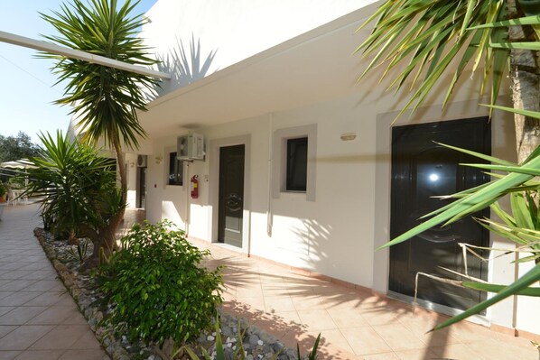 A building with a tiled walkway, palm trees, and a black door. - Golden View Studios (Rhodes)