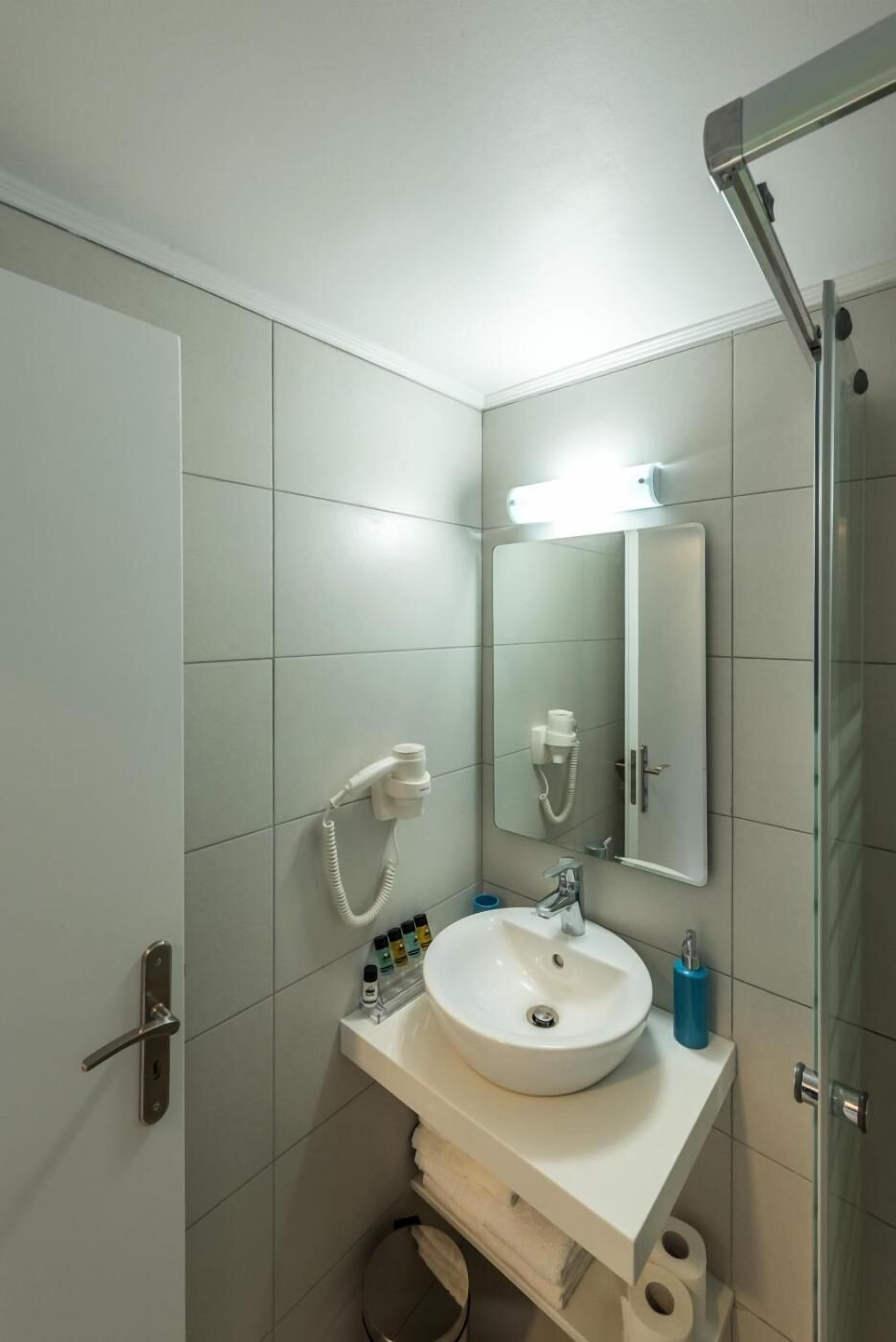A compact bathroom with a white sink, a mirror, a handheld showerhead, and a toilet.
